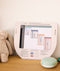 A portable white noise machine with a white base rests on a wooden surface next to a printed What to Wear guide showing room temperatures and appropriate sleepwear.