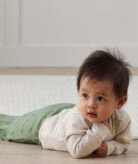 Infant crawling on it's stomach wearing ergoPouch Sleeping Sack with the added layer of Arm Warmers