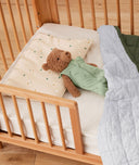 A teddy bear lying on  ergoPouch Organic Toddler Pillow Case in Daisy Sprinkle