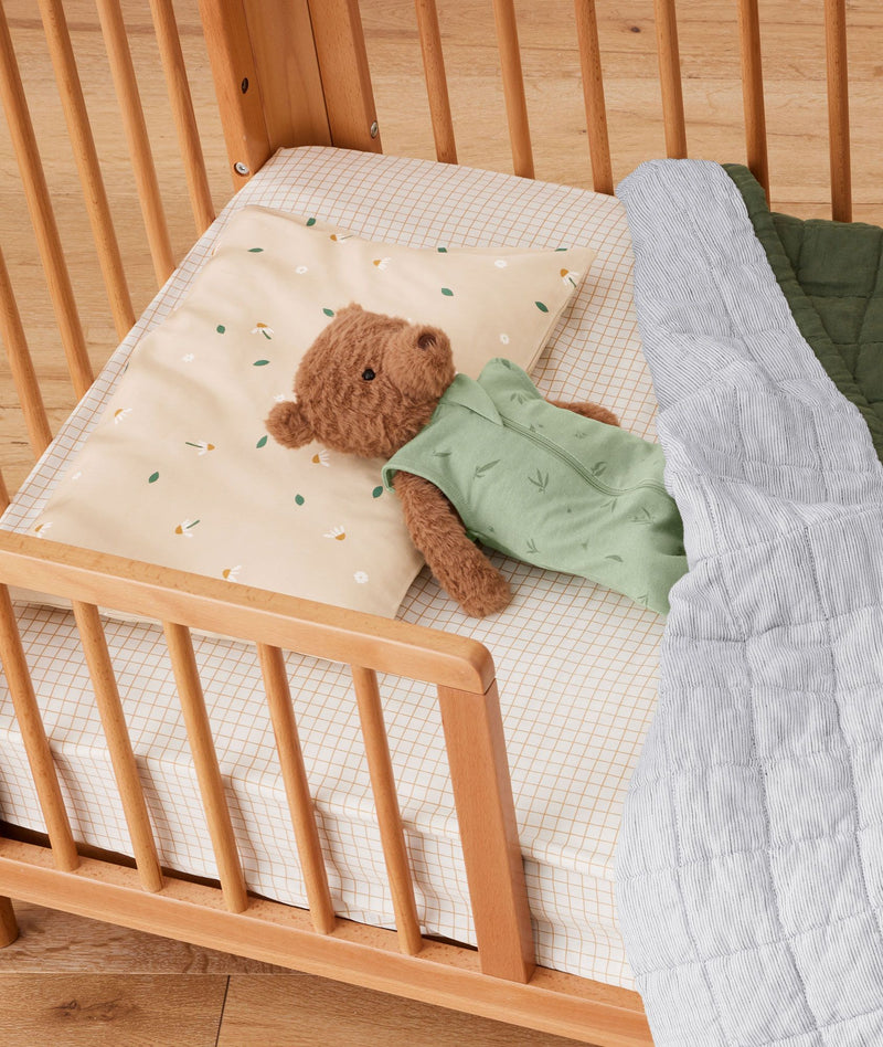 A teddy bear lying on  ergoPouch Organic Toddler Pillow Case in Daisy Sprinkle