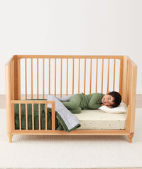 Toddler lying in crib on a ergoPouch Organic Toddler Pillow and Case Caramel Grid, designed to support the correct alignment of the neck during sleep