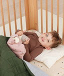 Toddler lying in crib on a ergoPouch Organic Toddler Pillow and Case Caramel Grid, designed to support the correct alignment of the neck during sleep