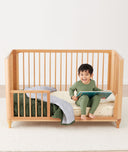 Toddler sitting on crib on a ergoPouch Organic Toddler Pillow and Case Caramel Grid, designed to support the correct alignment of the neck during sleep