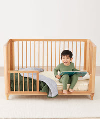 Toddler sitting on crib on a ergoPouch Organic Toddler Pillow and Case Caramel Grid, designed to support the correct alignment of the neck during sleep