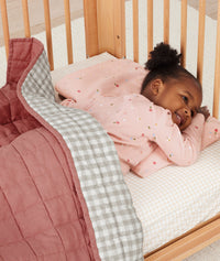 Toddler lying in crib on a ergoPouch Organic Toddler Pillow And Case Daisies, designed to support the correct alignment of the neck during sleep