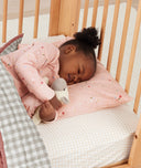 Toddler lying in crib on a ergoPouch Organic Toddler Pillow And Case Daisies, designed to support the correct alignment of the neck during sleep