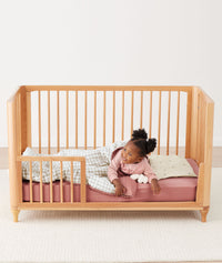 Toddler lying in crib on a ergoPouch Organic Toddler Pillow and Case Daisy Sprinkle, designed to support the correct alignment of the neck during sleep
