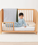 Toddler sitting on crib on a ergoPouch Organic Toddler Pillow and Case Daisy Sprinkle, designed to support the correct alignment of the neck during sleep