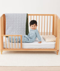 Toddler sitting on crib on a ergoPouch Organic Toddler Pillow and Case Daisy Sprinkle, designed to support the correct alignment of the neck during sleep