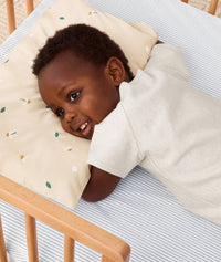 Toddler lying in crib on a ergoPouch Organic Toddler Pillow and Case Daisy Sprinkle, designed to support the correct alignment of the neck during sleep