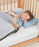 Toddler lying in crib on a ergoPouch Organic Toddler Pillow And Case Dragonflies, designed to support the correct alignment of the neck during sleep