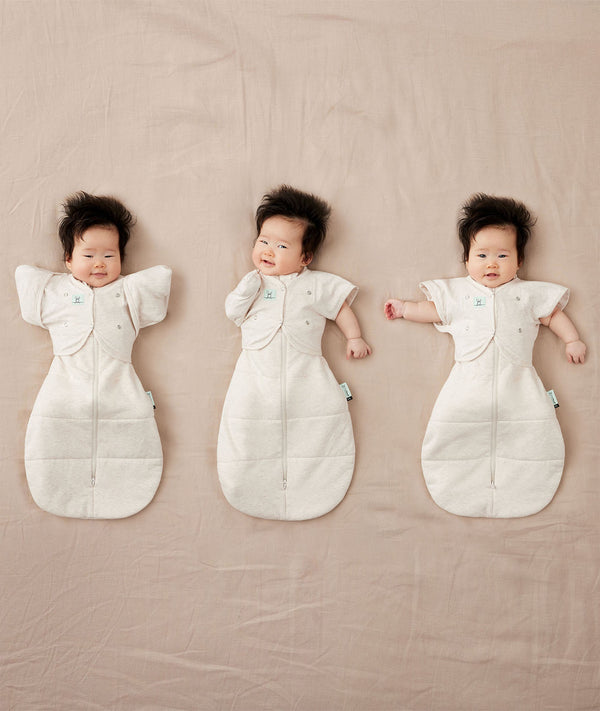 Newborns being swaddled in ergoPouch Cocoon Swaddle Sack 1.0 TOG Oatmeal Marle with Butterfly Cardi Oatmeal Marle for arms up sleeping, transitioning to arms out