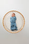 A baby lies on a round, woven rattan bassinet, wearing a blue zip-up cocoon swaddle sack
