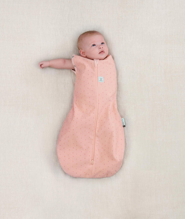 Newborn wearing ergoPouch Cocoon Swaddle Sack 0.2 TOG Berries, transitioning to arms out sleeping