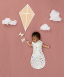 Newborn asleep in ergoPouch Cocoon Swaddle Sack 0.2 TOG Daydream, arms out sleeping, with a geometric kite and clouds
