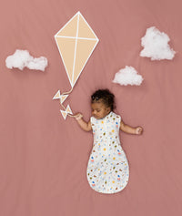 Newborn asleep in ergoPouch Cocoon Swaddle Sack 0.2 TOG Daydream, arms out sleeping, with a geometric kite and clouds