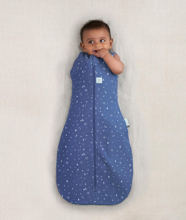Newborn wearing ergoPouch Cocoon Swaddle Sack 0.2 TOG Night Sky, transitioning to arms out sleeping