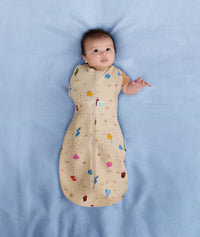 Baby wearing an ergoPouch Cocoon Swaddle Sack 1.0 TOG Birthday Blobs with one arm out