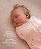 Close up of a newborn being swaddled in ergoPouch Cocoon Swaddle Sack 1.0 TOG Daisies with text highlighting swaddling benefit and TOG rating feature.