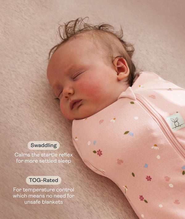 Close up of a newborn being swaddled in ergoPouch Cocoon Swaddle Sack 1.0 TOG Daisies with text highlighting swaddling benefit and TOG rating feature.