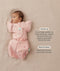 Baby lying on a beige surface in a pink floral swaddle paired with a 