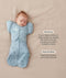 Baby lying on a beige surface in a blue dragonfly-pattern swaddle sack paired with a 
