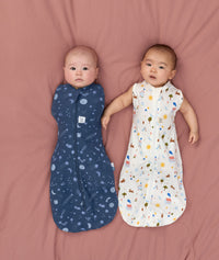 Two babies lying down, one being swaddled in an ergoPouch Cocoon Swaddle Sack1.0 TOG Starbeam, the other, trainsitioned to arms out sleeping in ergoPouch Cocoon Swaddle Sack1.0 TOG Daydream 