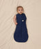 Baby lying on a beige blanket wearing an ergoPouch Cocoon Swaddle Sack 1.0 TOG, transitioning to arms out sleeping