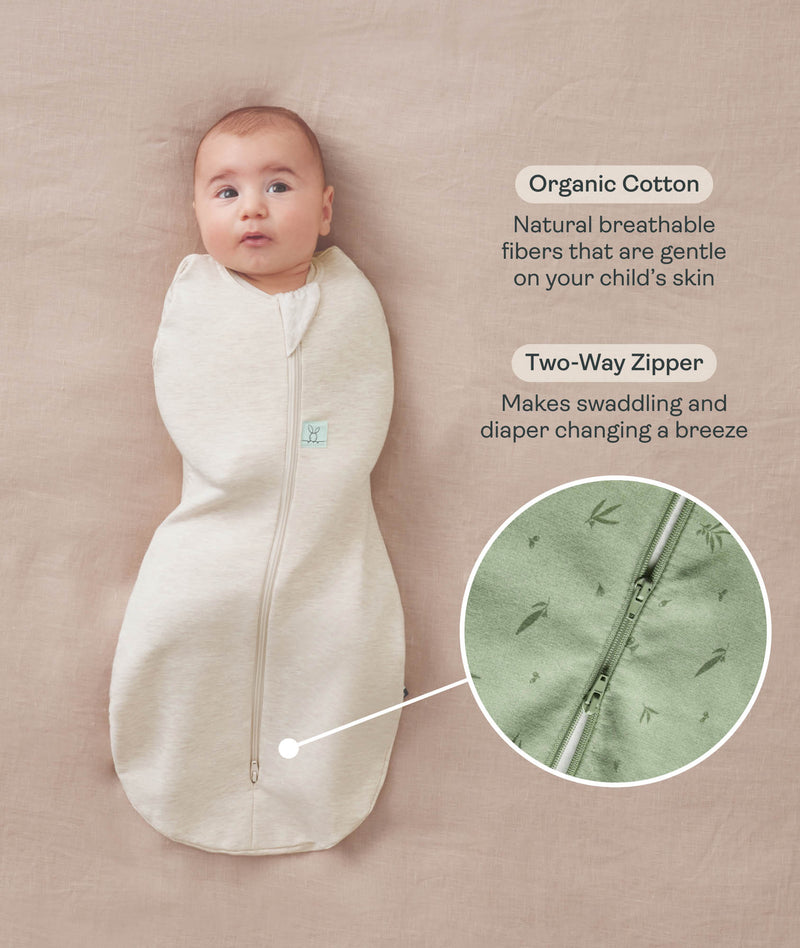 Baby lying on a beige surface wrapped in a Cocoon Swaddle Sack with text highlighting organic cotton fabric and two-way zipper and a close-up inset of the dual zippers. 