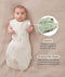Baby lying on a beige fabric in an oatmeal-colored swaddle sack with arms out, featuring callout text highlighting armhole poppers and a bell-shaped design.
