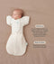 Baby lying on a beige surface in an oatmeal-colored swaddle sack paired with a 