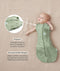 Baby lying on a beige surface in a green patterned swaddle sack with arms out, featuring callout text highlighting armhole poppers and a bell-shaped design.