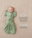 Baby lying on a beige surface in a green patterned swaddle paired with a 