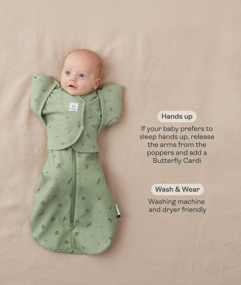 Baby lying on a beige surface in a green patterned swaddle paired with a 