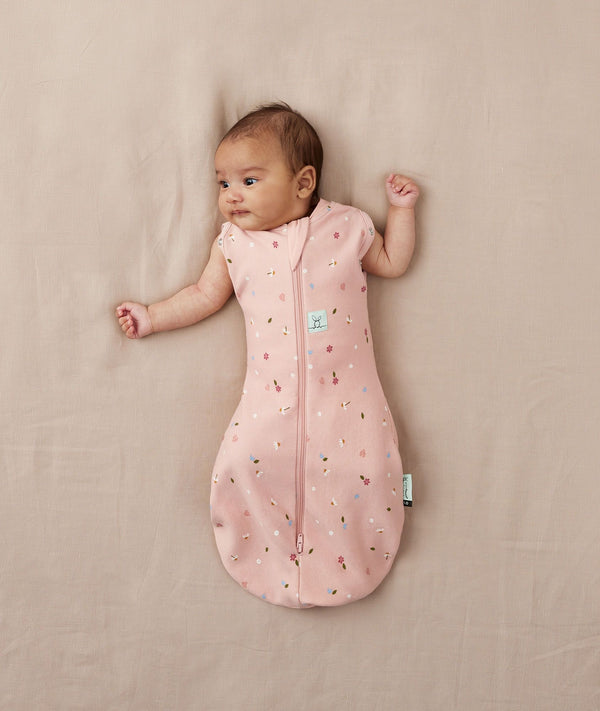 Newborn wearing ergoPouch Cocoon Swaddle Sack 0.2 TOG Daisies, transitioning to arms out sleeping