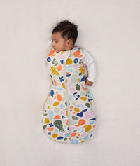 Newborn wearing ergoPouch Cocoon Swaddle Sack 2.5 TOG Fruit Salad, transitioning to arms out sleeping