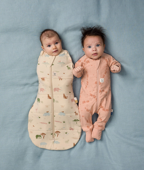 Two babies lying in bed wearing Cocoon Swaddle Sack and Long Sleeve Layer