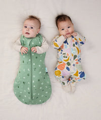 Two babies lying in ergoPouch Cocoon Swaddle Sack 2.5 TOG Sweet Orchard and Long Sleeve Romper 1.0 TOG Fruit Salad, warm for the winter