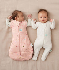 Two babies lying on their backs, one wearing an ergoPouch Cocoon Swaddle Sack 2.5 TOG Dasies with arm out sleeping, and the other in a Long Sleeve Romper Oatmeal Marle
