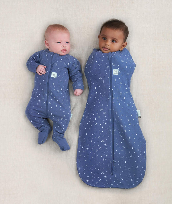 Two newborns wearing ergoPouch Cocoon Swaddle Sack 0.2 TOG and Long Sleeve Romper in Night Sky