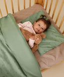 Toddler lying in bed resting their head on the ergoPouch toddler pillow case in Willow