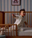 Child sitting in a wooden crib with Organic Toddler Pillow and Case Daydream, wearing a Sleep Suit Sack 1.0 TOG Daydream.