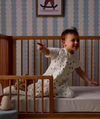 Child sitting in a wooden crib with Organic Toddler Pillow and Case Daydream, wearing a Sleep Suit Sack 1.0 TOG Daydream.