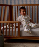 Child sitting in a wooden crib with Organic Toddler Pillow and Case Daydream, wearing a Sleep Suit Sack 1.0 TOG Daydream.
