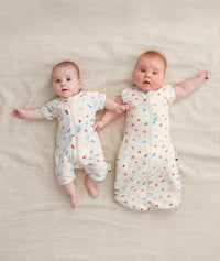 Two newborns wearing ergoPouch Cocoon Swaddle Sack 0.2 TOG and Short Sleeve Romper in Desert Bloom
