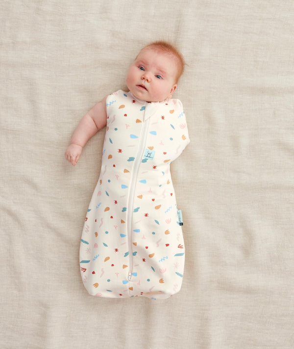 Newborn in a ergoPouch Cocoon Swaddle Sack 1.0 TOG Desert Bloom, transitioning to arms out sleeping 