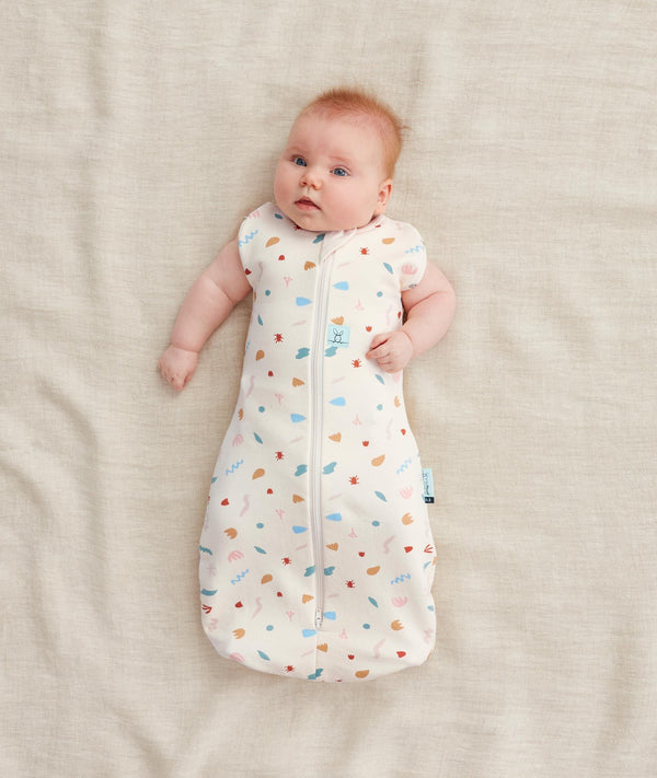 Newborn in a ergoPouch Cocoon Swaddle Sack 1.0 TOG Desert Bloom, transitioning to arms out sleeping 