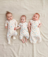 Three babies wearing ergoPouch Cocoon Swaddle Sack 1.0 TOG, Short Sleeve Romper, Long Sleeve Romper in Desert Bloom