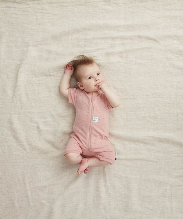 Newborn baby lying on her back wearing a ergoPouch Short Sleeve Romper 0.2 TOG Berries