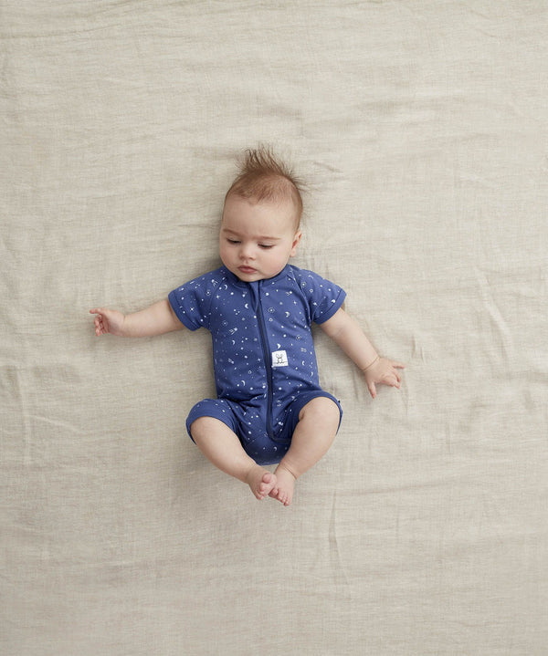 Infant lying with knees up in a ergoPouch Short Sleeve Romper 0.2 TOG Night Sky